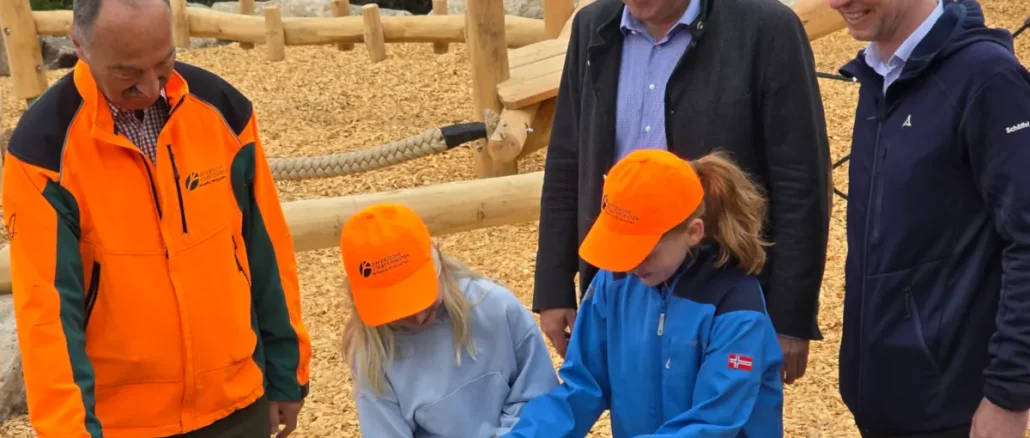 Zwei Kinder schneiden mit einer Schere das Absperrband zur Eröffnung des Spielplatzes durch. Links daneben steht Winfried Pfahler, dahinter Martin Schöffel, rechts Florian Wiedemann